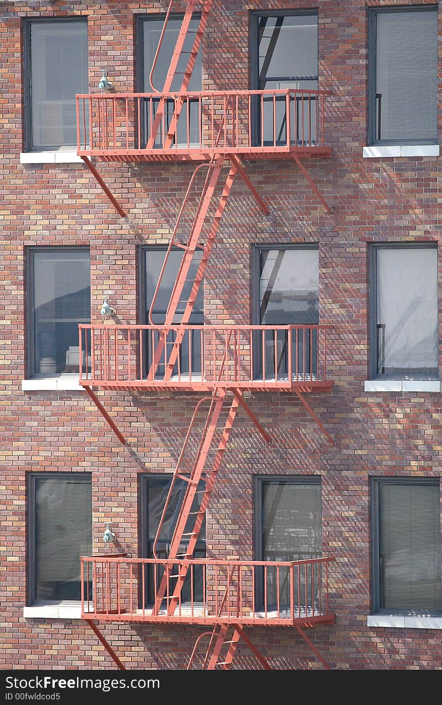 A red steel fire escape descending a red brick building