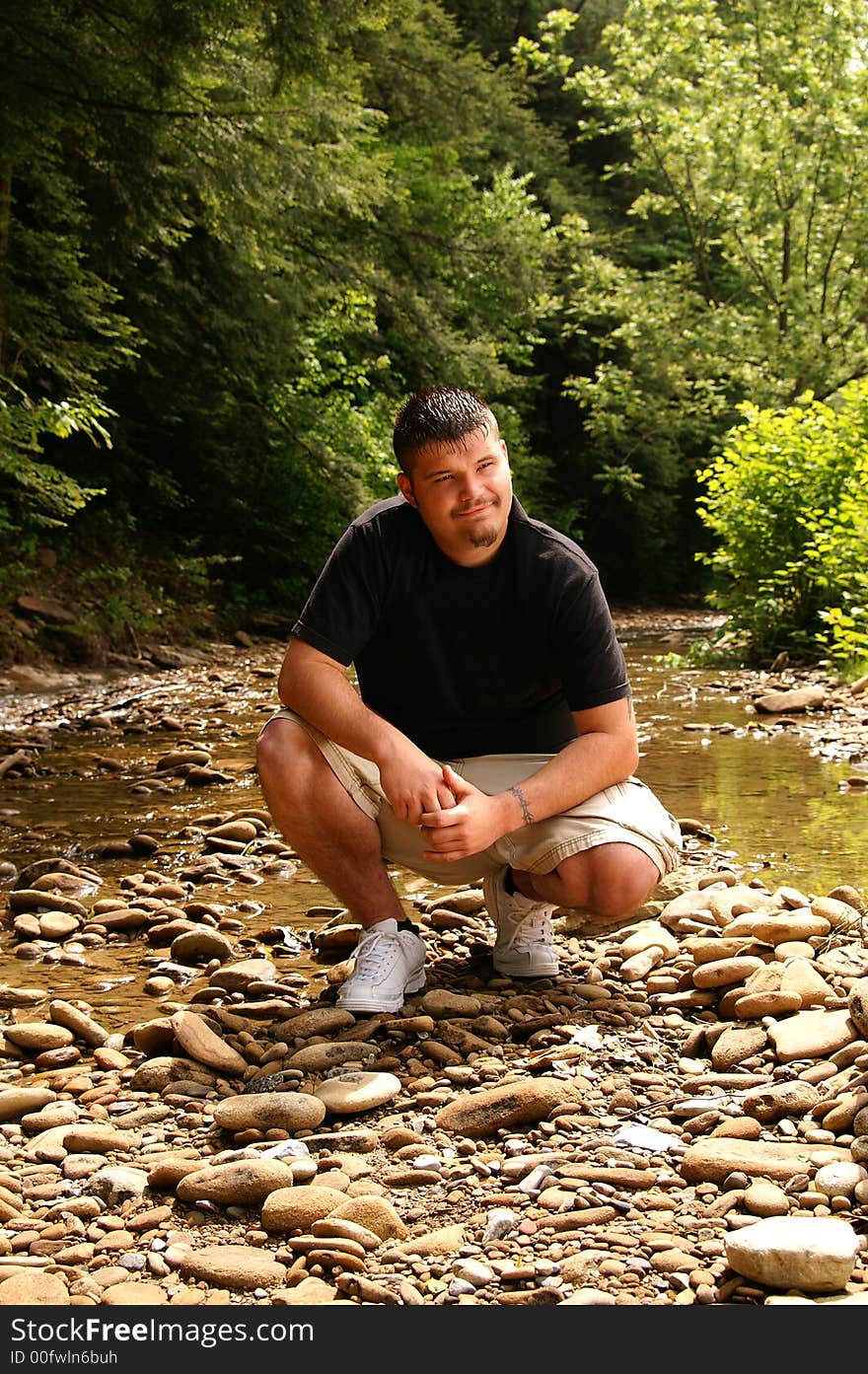 A handsome young man sitting by a creek. A handsome young man sitting by a creek