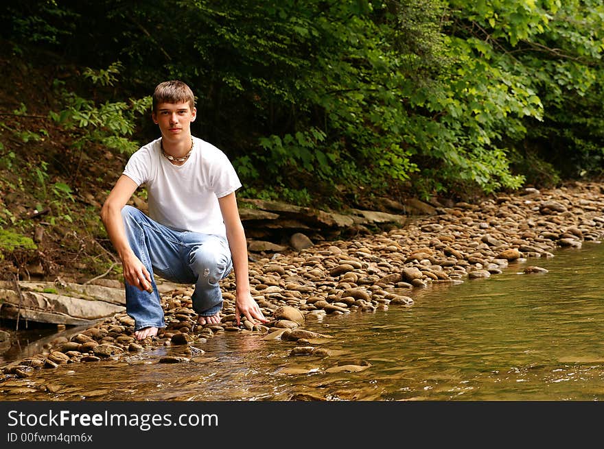 A handsome young teenage boy kneeling by a creek. A handsome young teenage boy kneeling by a creek