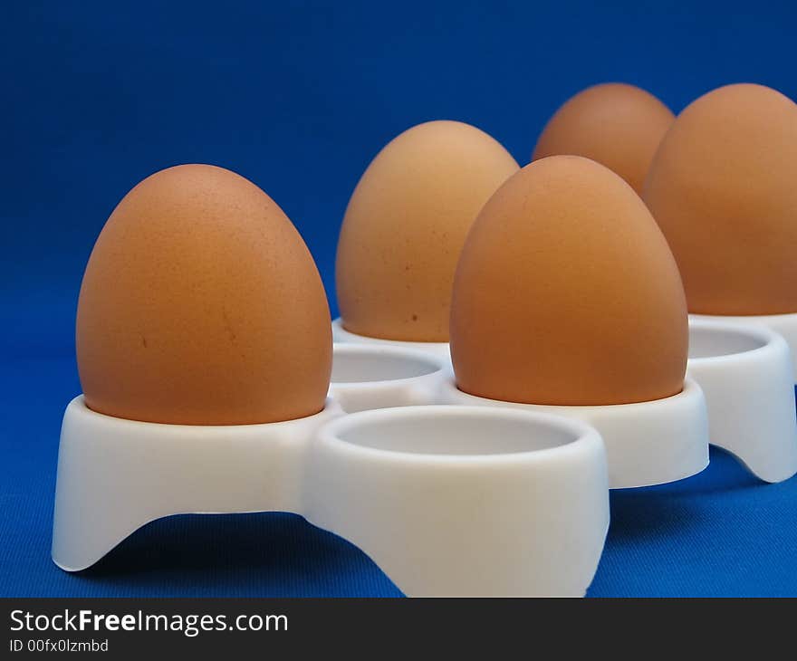 Closeup eggs in a white eggcup on the blue background. Closeup eggs in a white eggcup on the blue background