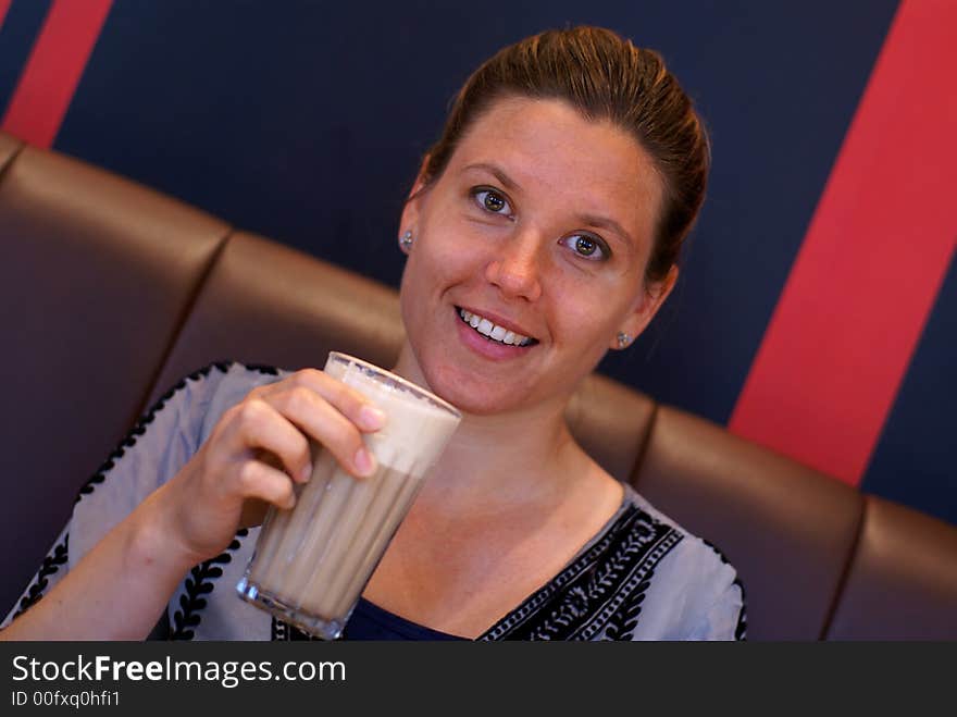 A young woman drinks a warm coffee with foamed milk and smiles at the camera. A young woman drinks a warm coffee with foamed milk and smiles at the camera