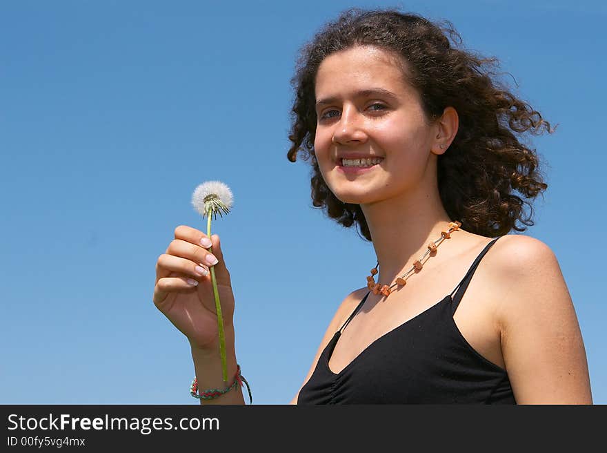 Nice young girl blowing on a dandelion on a background of the blue sky. Nice young girl blowing on a dandelion on a background of the blue sky