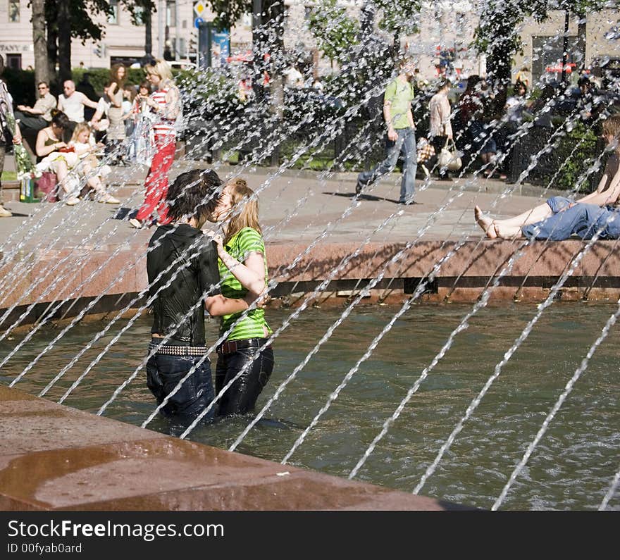 A boy and a girl are kissing standing in a fountain. A boy and a girl are kissing standing in a fountain