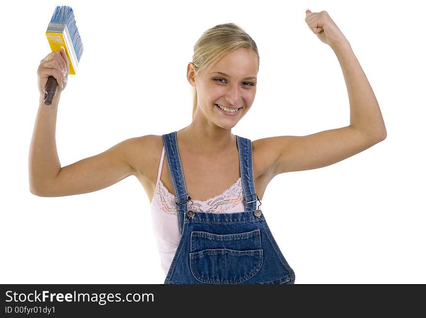 Young smiling blonde wearing dungarees with paintbrush in hand. Showing her satisfaction by hands up. Isolated on white in studio. looking at camera. Young smiling blonde wearing dungarees with paintbrush in hand. Showing her satisfaction by hands up. Isolated on white in studio. looking at camera.