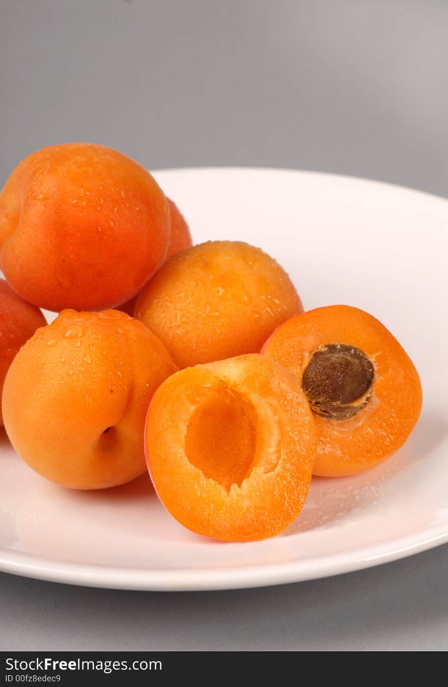 Vertical of several apricots on a white plate with one cut in half