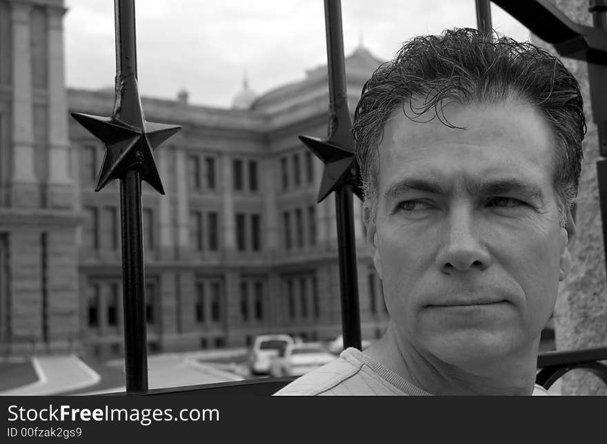 Black and white photo of a man standing in front of a gate with a crafty or shrewd looking expression on his face. Black and white photo of a man standing in front of a gate with a crafty or shrewd looking expression on his face.