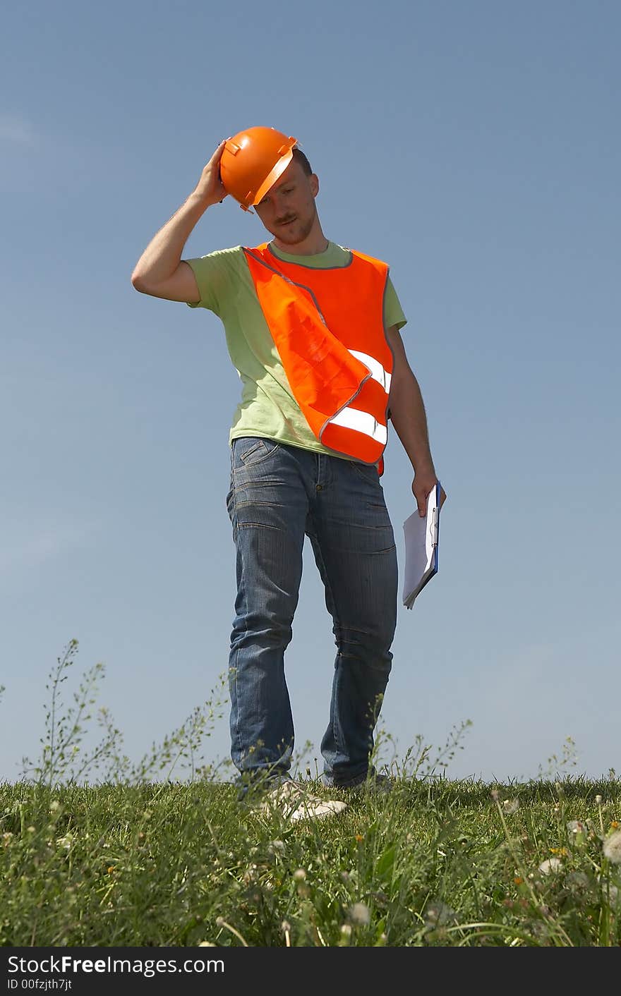 Man in clothes of the builder on a grass on a background of the dark blue sky. Man in clothes of the builder on a grass on a background of the dark blue sky