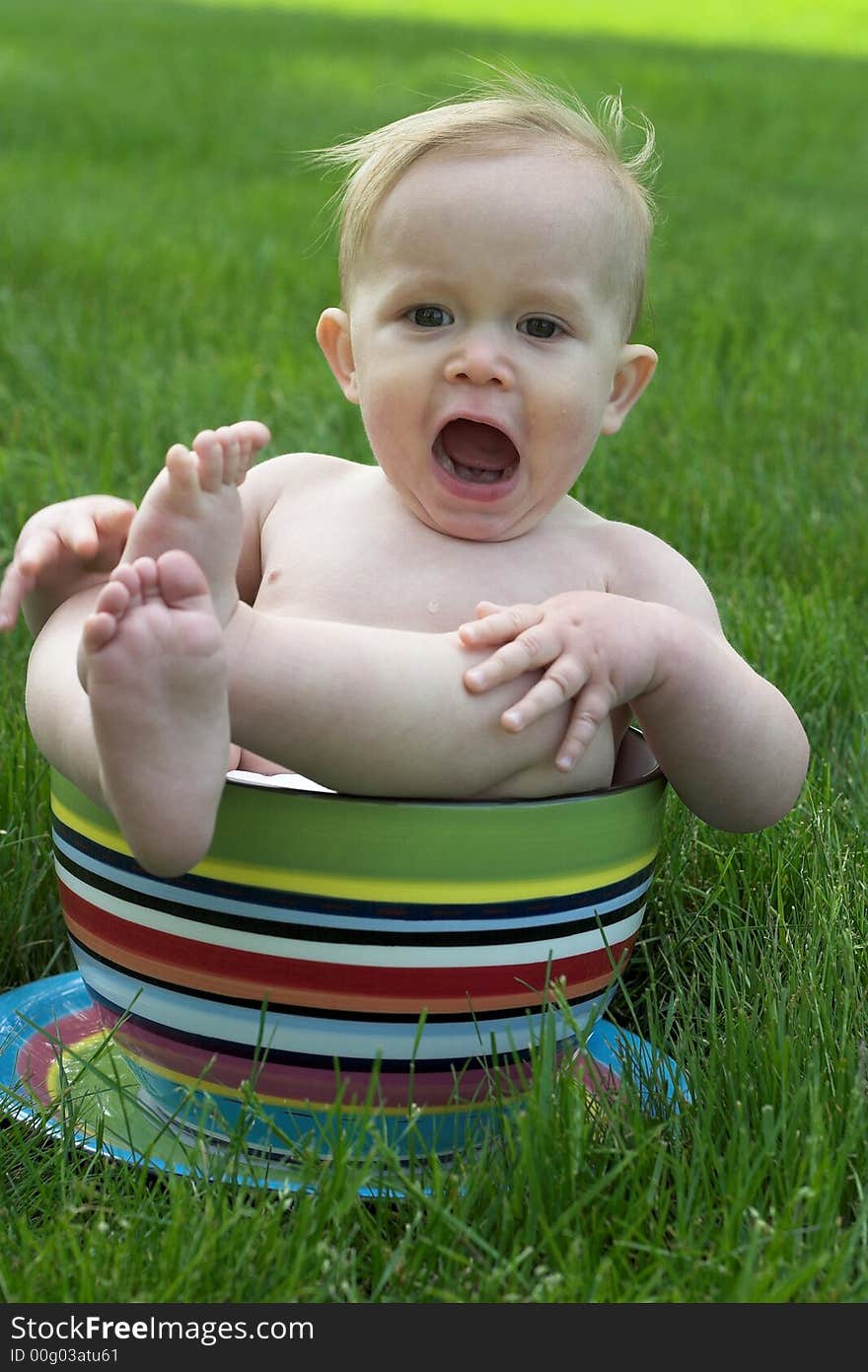 Image of an adorable baby sitting in a colorful, over-sized teacup in the grass. Image of an adorable baby sitting in a colorful, over-sized teacup in the grass