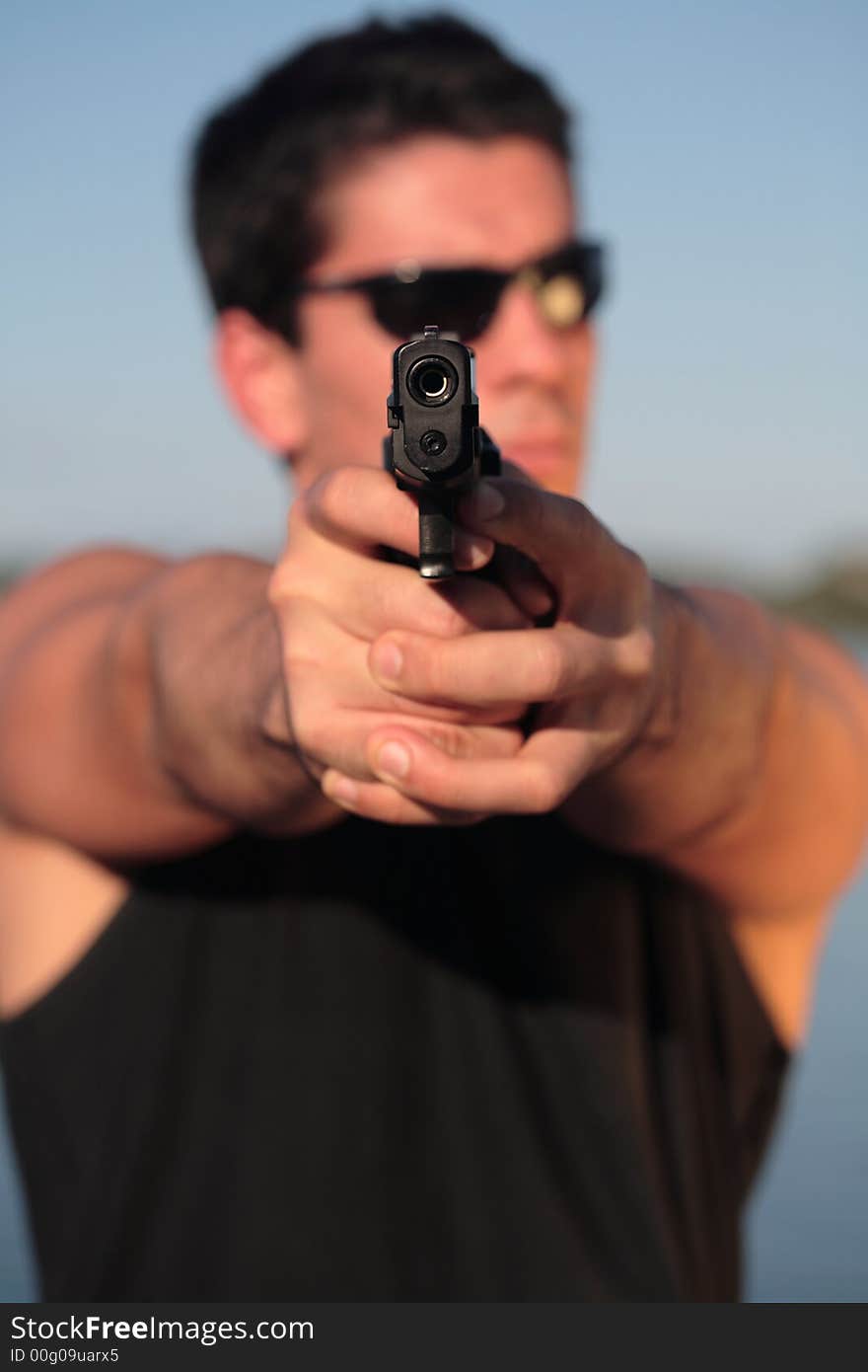 A man holding a pistol and pointing it at the camera. (This image is part of a series). A man holding a pistol and pointing it at the camera. (This image is part of a series).