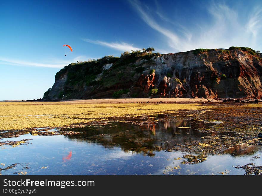 Lonely paraglider is flying above the reflecting rock.