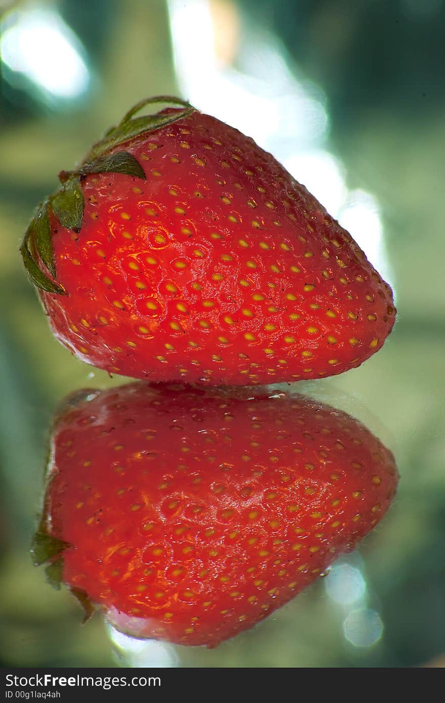 A red strawberry on a mirror and soft background.