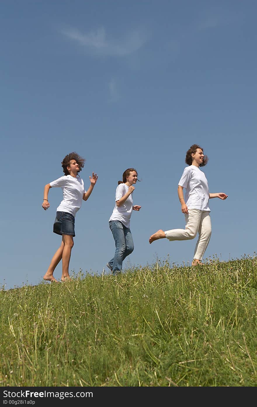 Three young nice girls running on a green grass on a background of the blue sky. Three young nice girls running on a green grass on a background of the blue sky