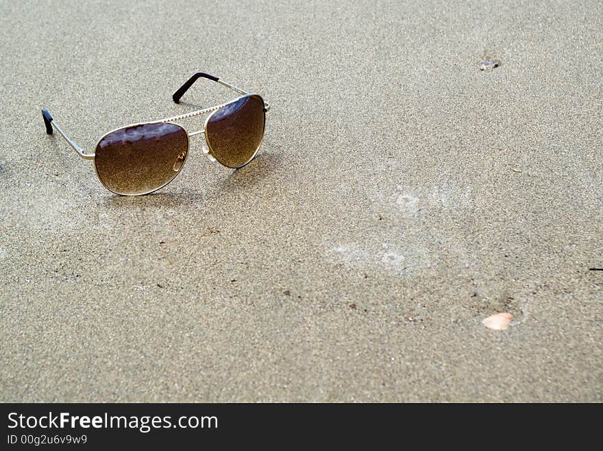 Sunglasses on wet sand. Concept for vacation and traveling.