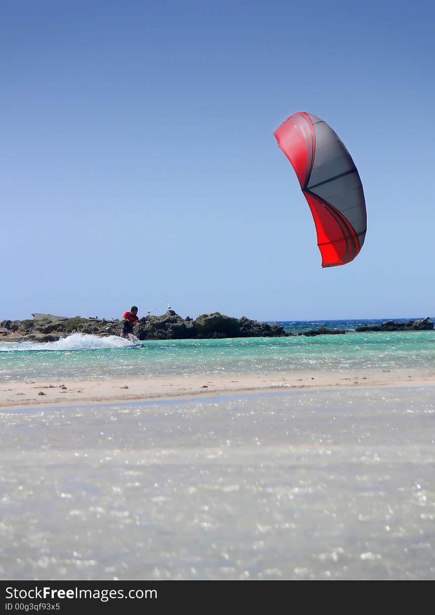 A kitesurfer with a red kite surfing the shoreline of Creete Greece. A kitesurfer with a red kite surfing the shoreline of Creete Greece