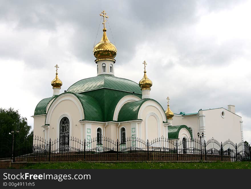 White Christian church with the gilt domes and a green roof.