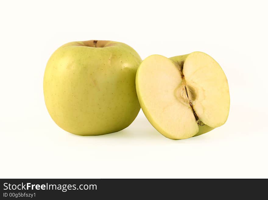 The yellow apple and half of apple are photographed on a white background. The yellow apple and half of apple are photographed on a white background