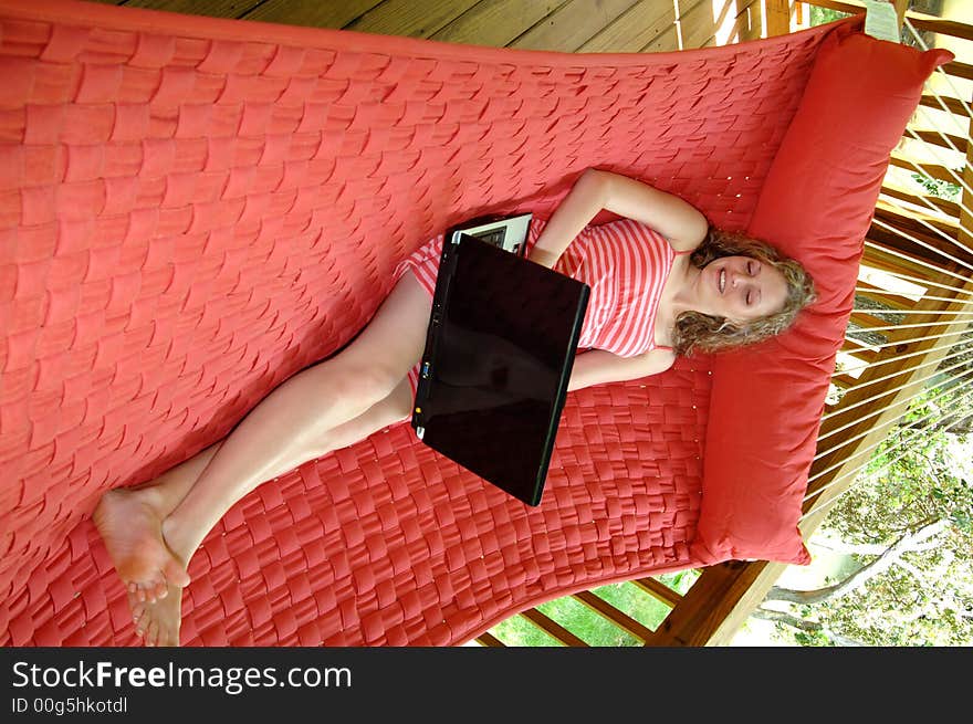 A pretty girl lounging in a hammock on a porch working on her laptop. A pretty girl lounging in a hammock on a porch working on her laptop