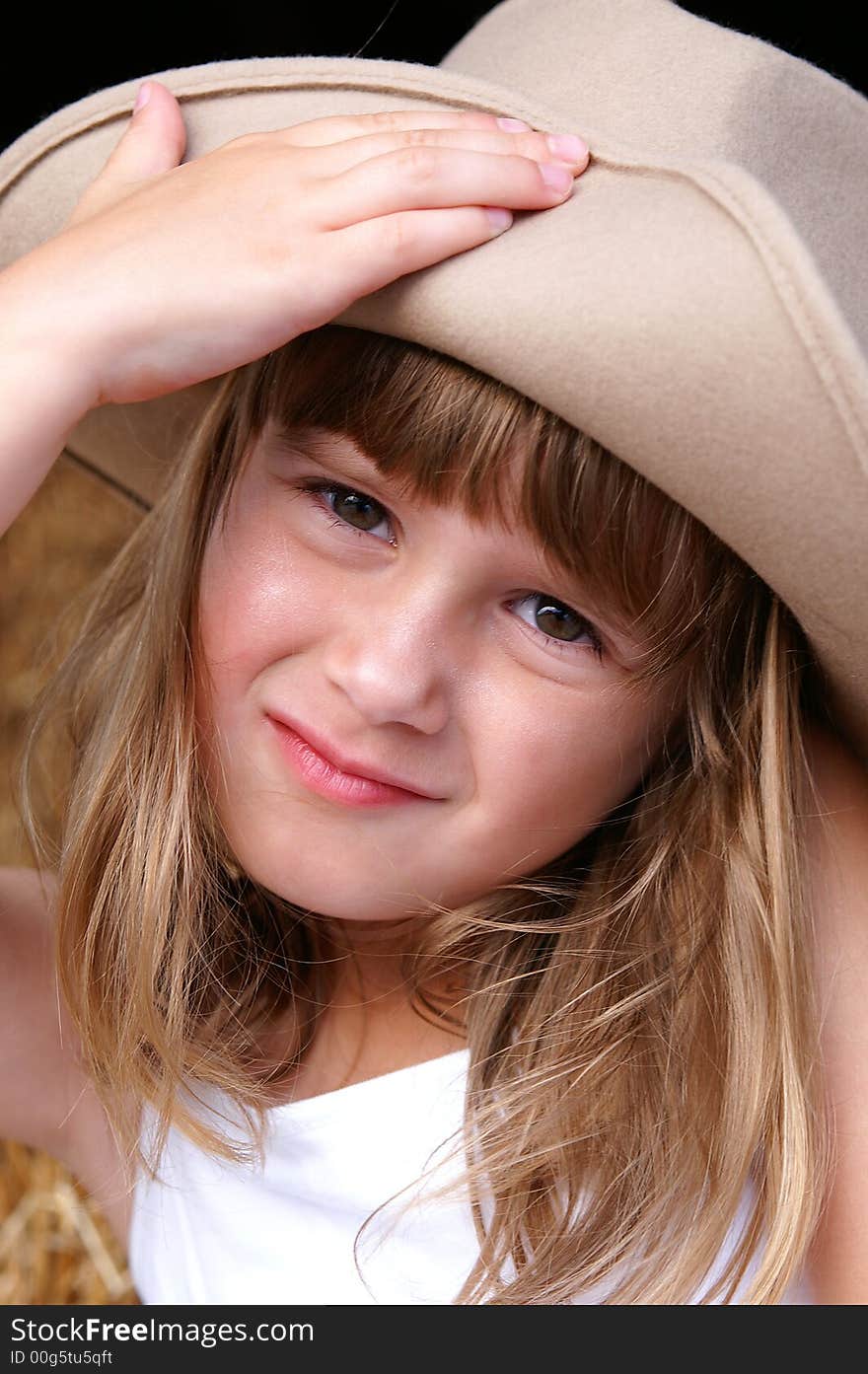 A cute young girl in a cowgirl hat sitting on haybales in a barn