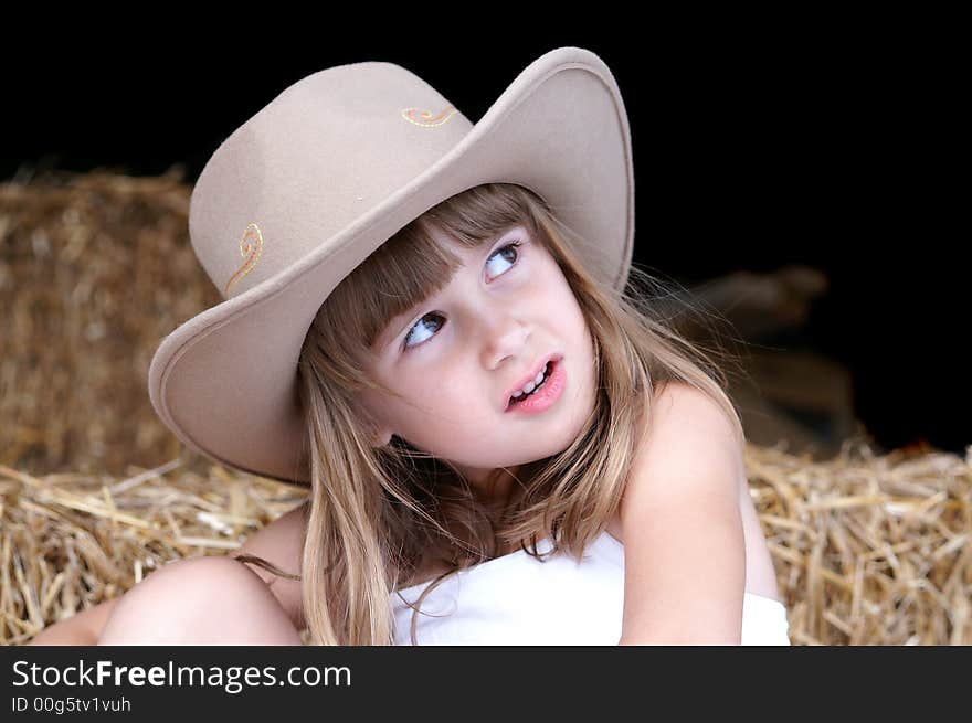 A cute young girl in a cowgirl hat sitting on haybales in a barn. A cute young girl in a cowgirl hat sitting on haybales in a barn