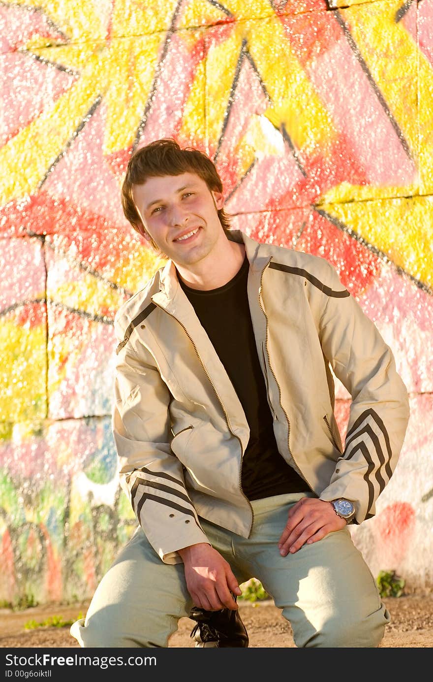 Happy young man sitting next the painted wall. Happy young man sitting next the painted wall