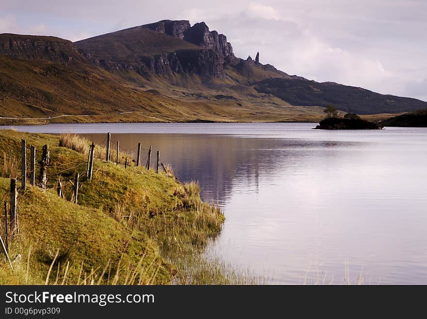 The Old Man of Storr on the Isle of Skye taken over Loch Leathann. The Storr is reflected in the calm dawn waters of the loch. Morning sunlight lights the hills in a warm glow. The Old Man of Storr on the Isle of Skye taken over Loch Leathann. The Storr is reflected in the calm dawn waters of the loch. Morning sunlight lights the hills in a warm glow