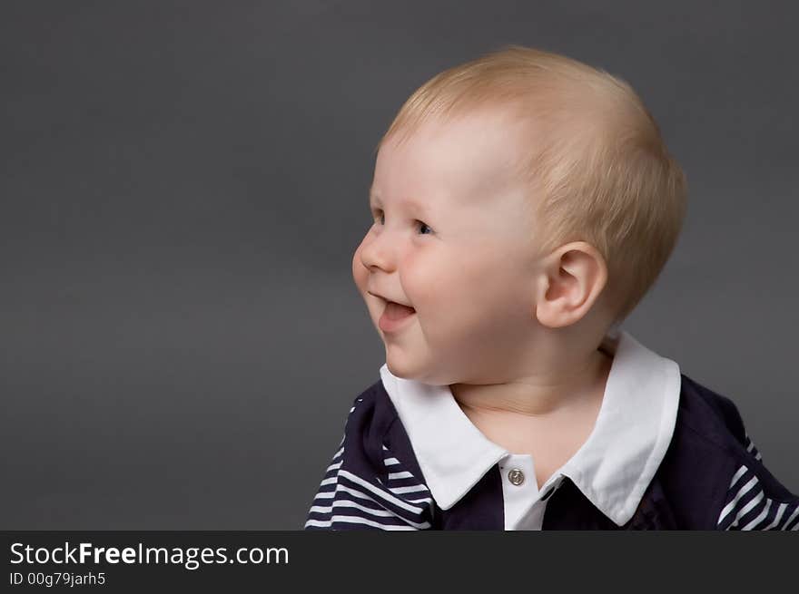 The small smiling child in studio, on a grey background. The small smiling child in studio, on a grey background