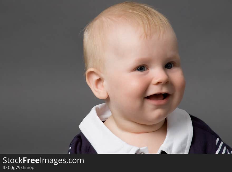 The small smiling child in studio, on a grey background. The small smiling child in studio, on a grey background