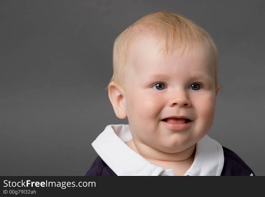 The small smiling child in studio, on a grey background. The small smiling child in studio, on a grey background