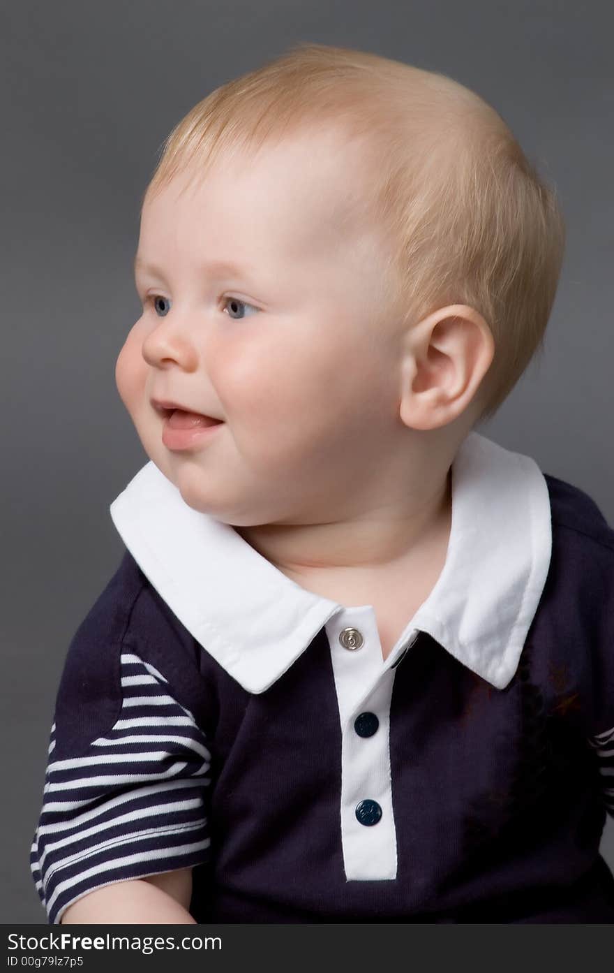 The small smiling child in studio, on a grey background. The small smiling child in studio, on a grey background