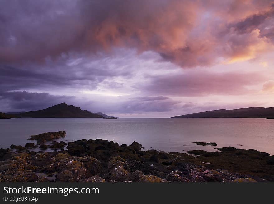 Sunrise reflected in the calm dawn waters of Loch Sligachan in the Isle of Skye, Scotland. scattered clouds reflect the early morning light in shades of purple, mauve and orange. Sunrise reflected in the calm dawn waters of Loch Sligachan in the Isle of Skye, Scotland. scattered clouds reflect the early morning light in shades of purple, mauve and orange