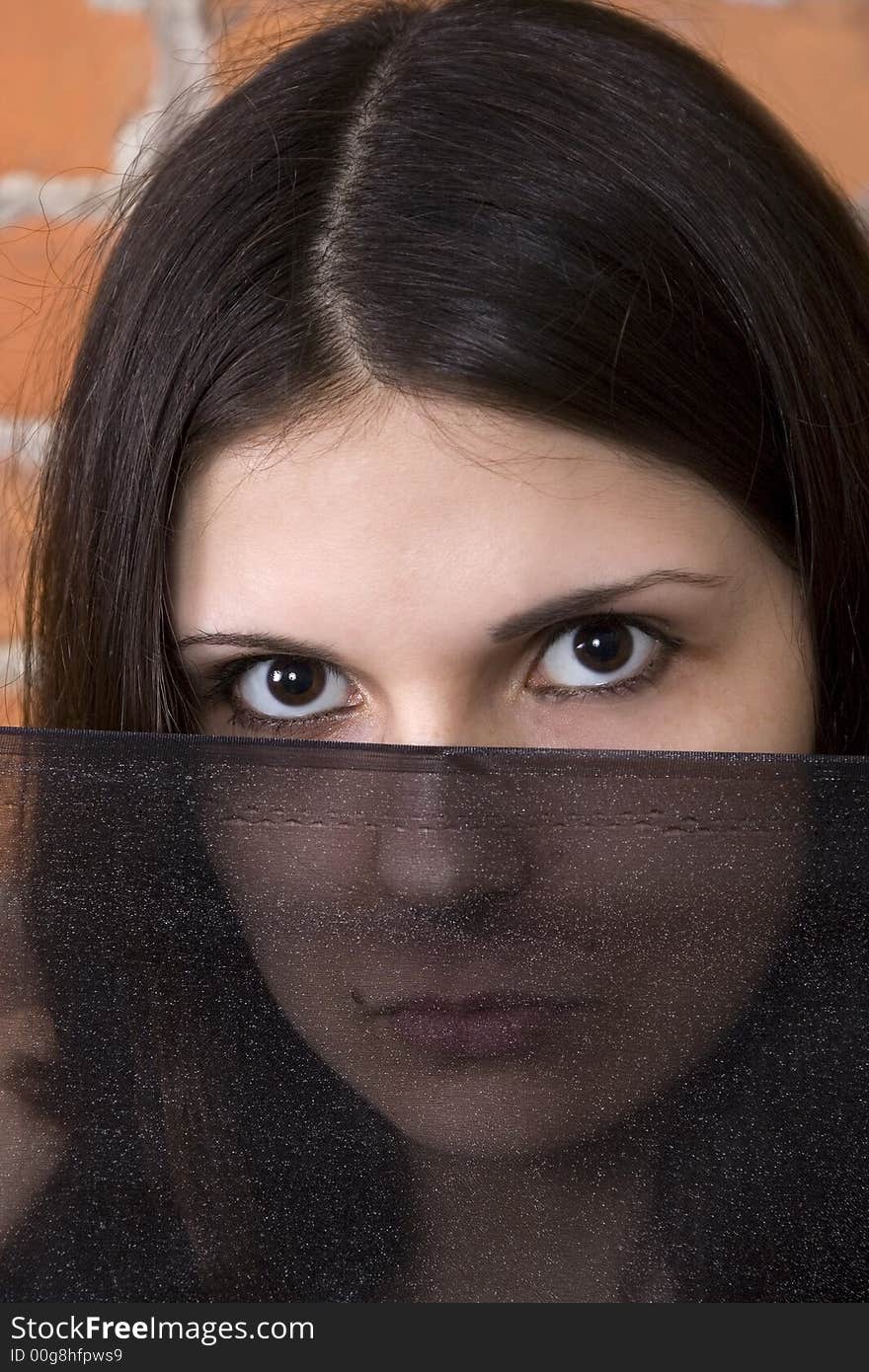 Beautiful young brunette woman face partially hidden by a veil. Brick background. Beautiful young brunette woman face partially hidden by a veil. Brick background.