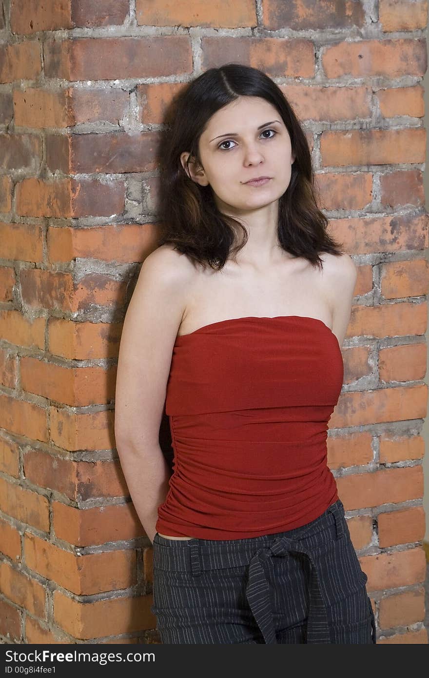 Beautiful young brunette woman standing in front of a brick wall wearing a red top and shorts. Beautiful young brunette woman standing in front of a brick wall wearing a red top and shorts.