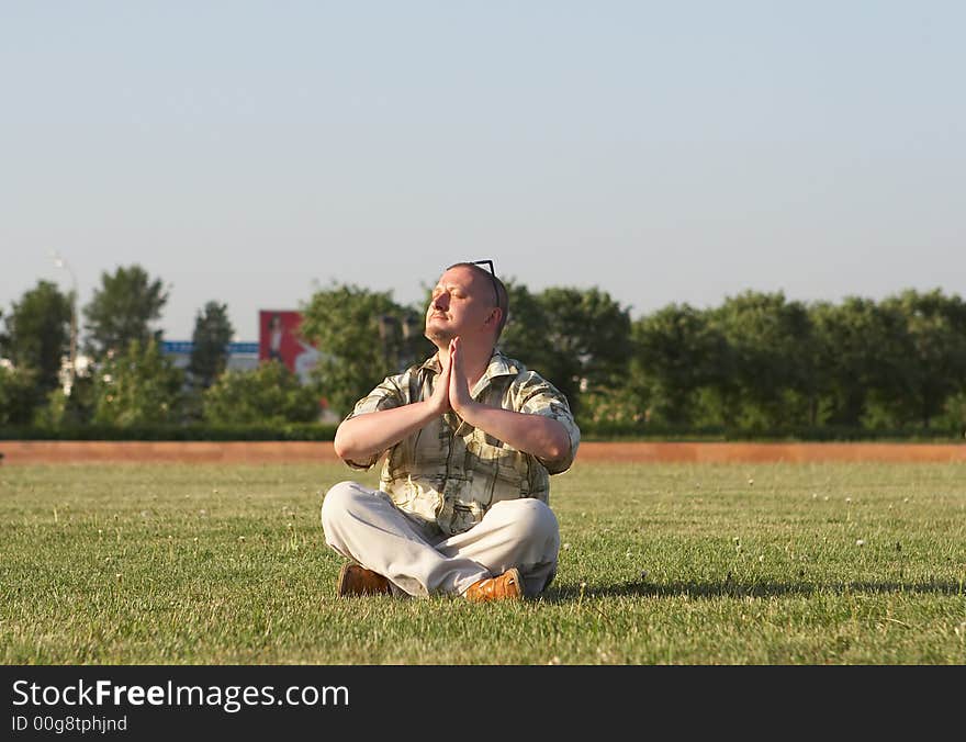 Man in sunglasses meditates sitting on a green grass. Man in sunglasses meditates sitting on a green grass