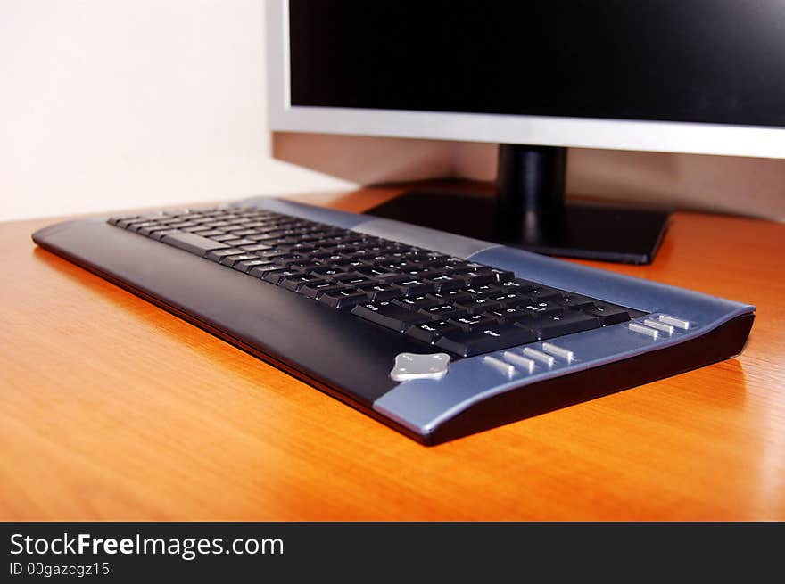 Black/dark grey computer keyboard, focus on keyboard and monitor out of focus. Black/dark grey computer keyboard, focus on keyboard and monitor out of focus