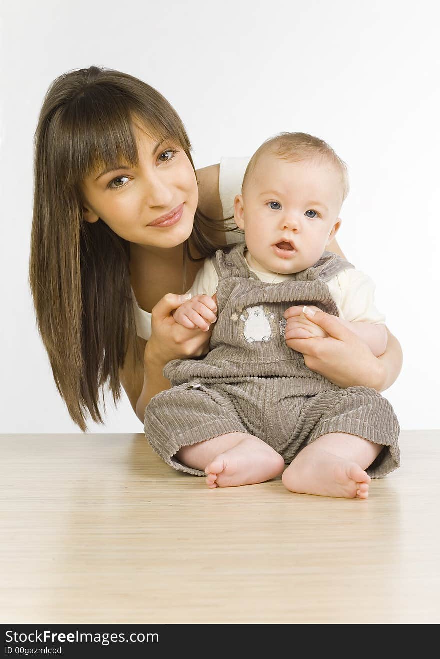 Young mother with baby boy. Baby is sitting on table. They looking at camera. Front view. Young mother with baby boy. Baby is sitting on table. They looking at camera. Front view