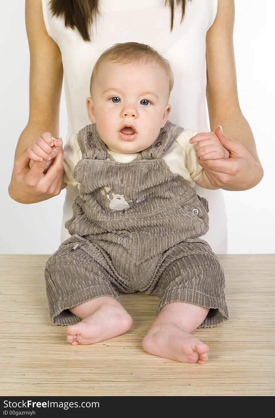 Young mother with baby boy. Baby is sitting on table. Looking at camera. Front view. Young mother with baby boy. Baby is sitting on table. Looking at camera. Front view