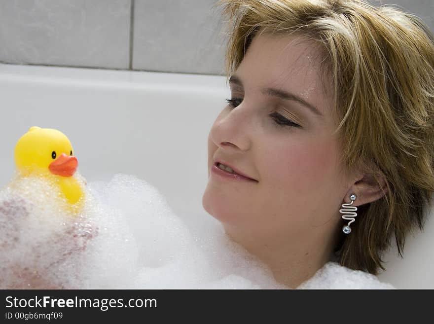 Attractive blond woman lying in bubble bath looking at her rubber ducky. Attractive blond woman lying in bubble bath looking at her rubber ducky