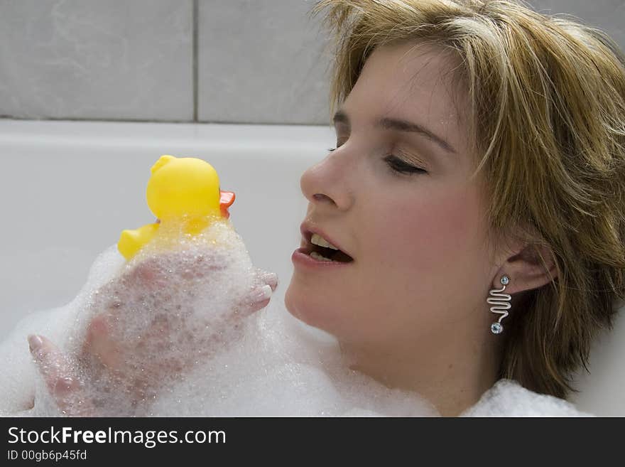 Attractive blond woman lying in bubble bath kissing her rubber ducky. Attractive blond woman lying in bubble bath kissing her rubber ducky