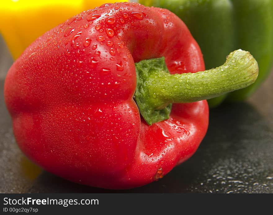 Freshly washed red bellpepper with green and yellow in the background. Freshly washed red bellpepper with green and yellow in the background