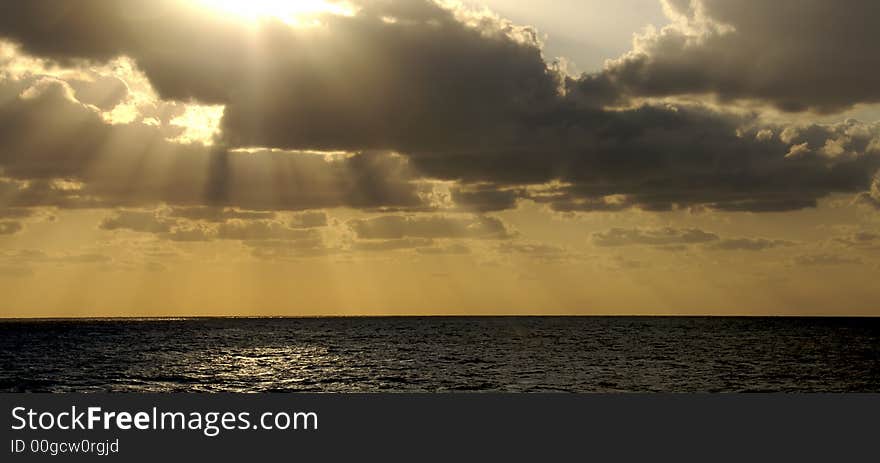 The golden rays of a sunset at sea bursts through the clouds. The golden rays of a sunset at sea bursts through the clouds