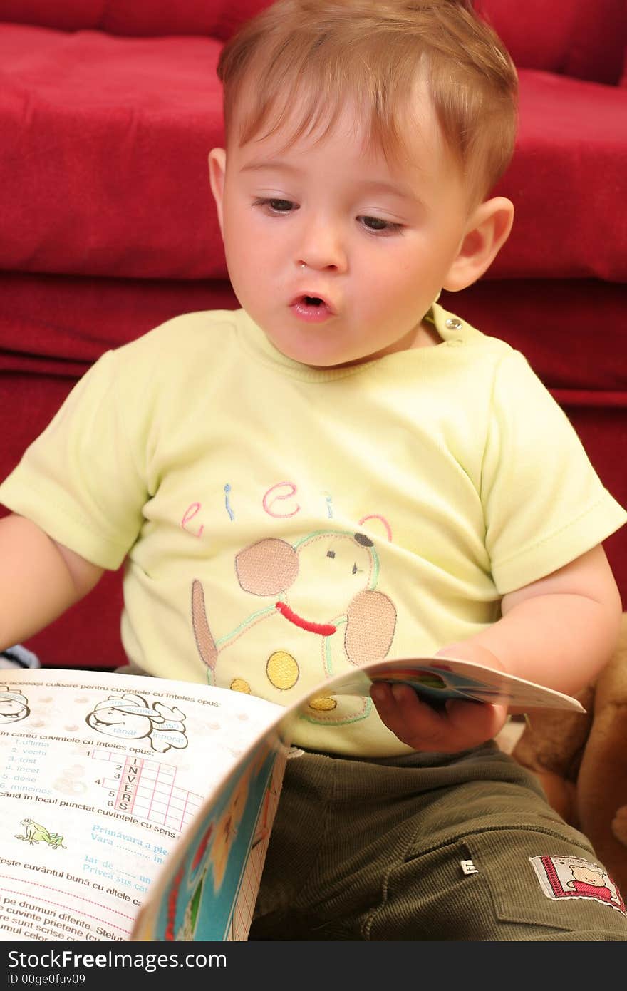 Expressive little blond baby boy gesticulate while reading a child book