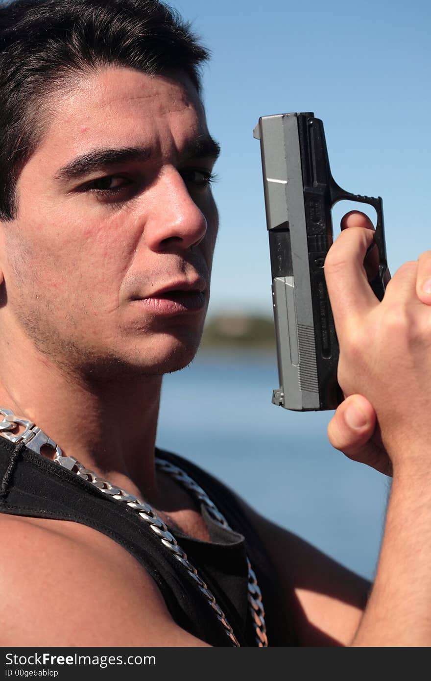 A young man, wearing a sleeveless shirt, holding a hand gun. (This image is part of a series). A young man, wearing a sleeveless shirt, holding a hand gun. (This image is part of a series)