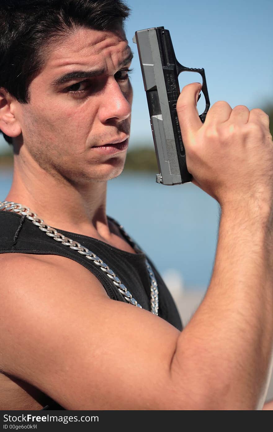 A young man, wearing a sleeveless shirt, holding a hand gun. (This image is part of a series). A young man, wearing a sleeveless shirt, holding a hand gun. (This image is part of a series)