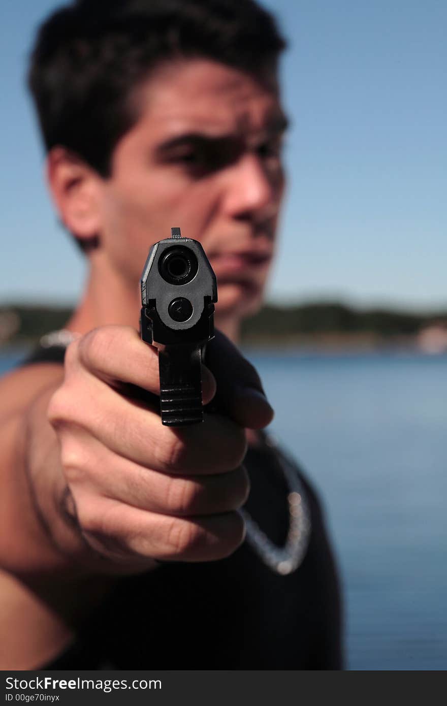 A young man, wearing a sleeveless shirt, holding a hand gun. (This image is part of a series). A young man, wearing a sleeveless shirt, holding a hand gun. (This image is part of a series)