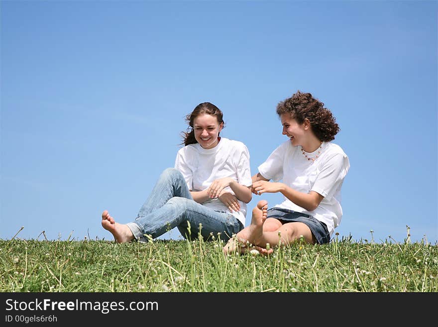 Two girlfriends in white T-shorts have a rest on a grass