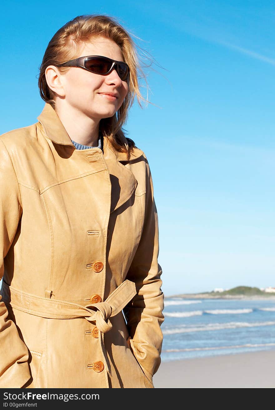 Blonde woman in a leather coat and sunglasses smiling. Blue sky in the background. Blonde woman in a leather coat and sunglasses smiling. Blue sky in the background.