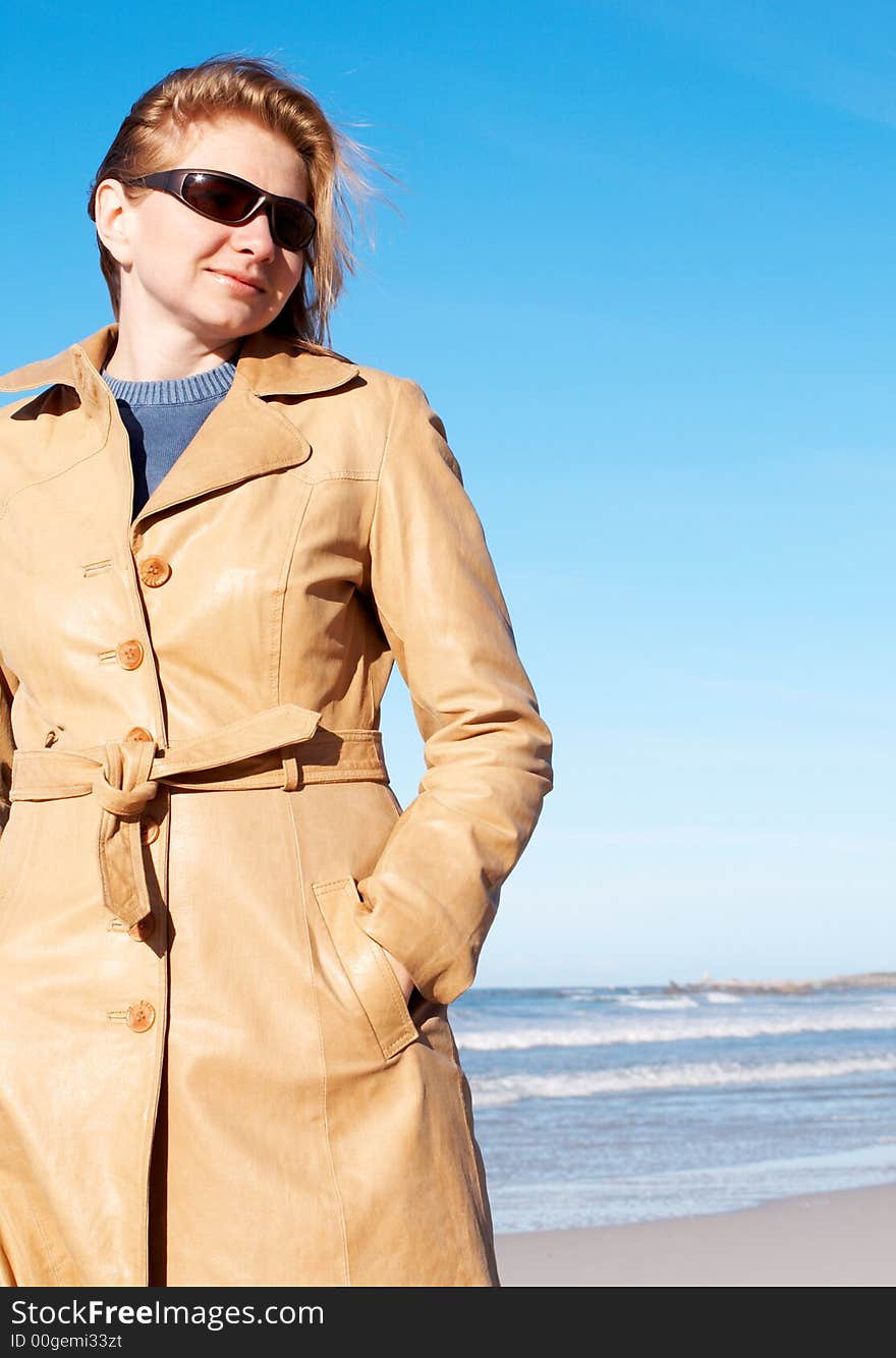 Blonde woman in a leather coat and sunglasses smiling. Blue sky in the background. Blonde woman in a leather coat and sunglasses smiling. Blue sky in the background.