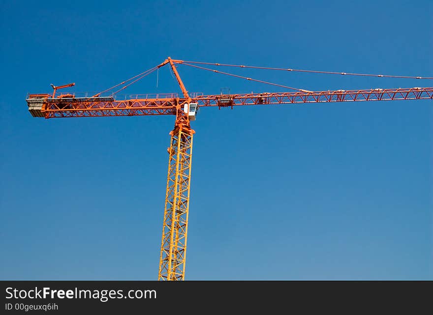 Construction crane in orange on a blue sky. Construction crane in orange on a blue sky