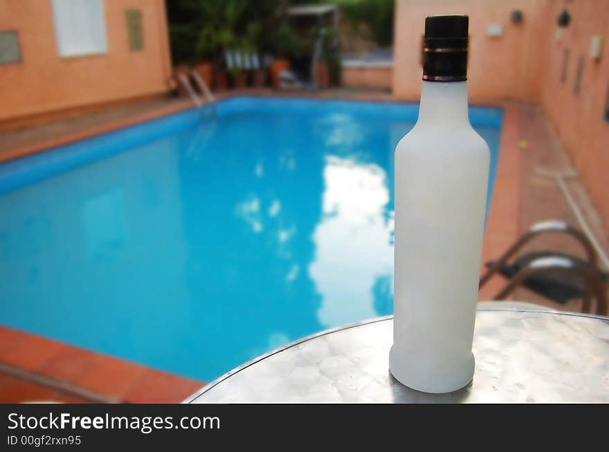 A bottle of alcohol on a table next to a pool