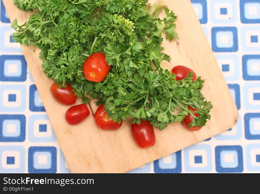 Bunch of parsley and cherry red tomatoes on wooden board and blue-squared mat. Bunch of parsley and cherry red tomatoes on wooden board and blue-squared mat.